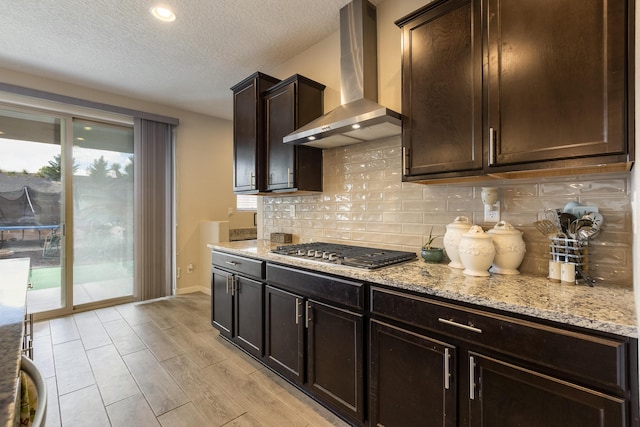 kitchen featuring stainless steel gas stovetop, a textured ceiling, light stone countertops, and wall chimney exhaust hood