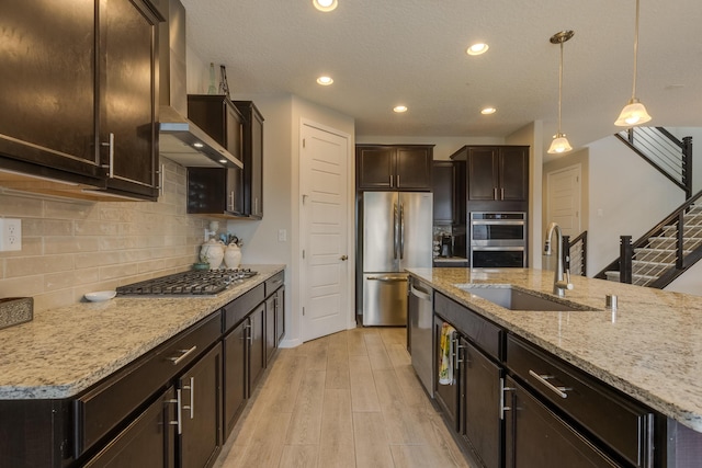 kitchen featuring dark brown cabinetry, decorative light fixtures, light wood-type flooring, a sink, and stainless steel appliances
