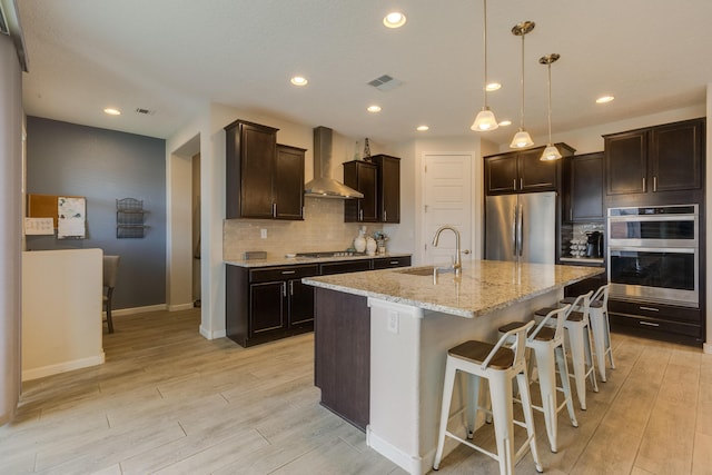 kitchen with visible vents, wall chimney range hood, light wood-type flooring, a sink, and appliances with stainless steel finishes