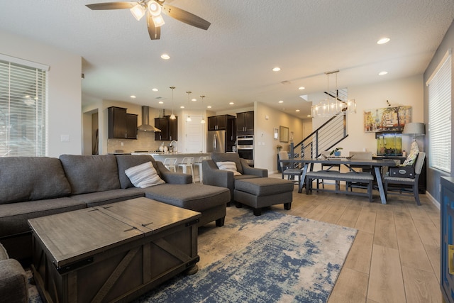 living room featuring a textured ceiling, ceiling fan with notable chandelier, stairs, recessed lighting, and light wood-type flooring