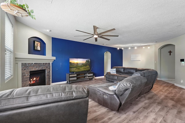 living room with arched walkways, a stone fireplace, a ceiling fan, and wood finished floors