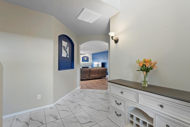 corridor featuring visible vents, marble finish floor, baseboards, a textured ceiling, and arched walkways