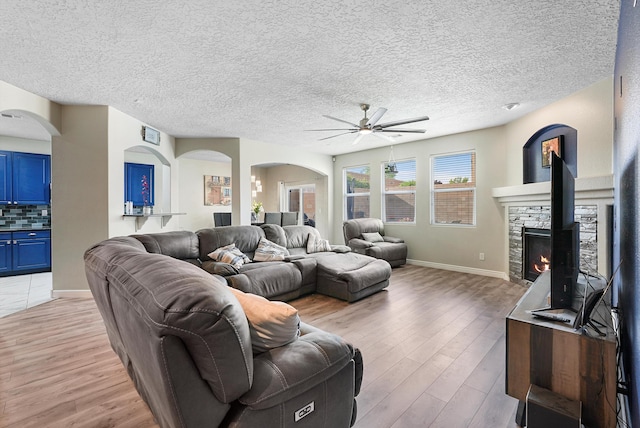 living room with a ceiling fan, baseboards, a stone fireplace, and light wood-style floors
