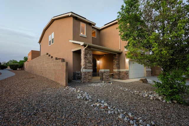 back of property featuring stucco siding, an attached garage, fence, and stone siding