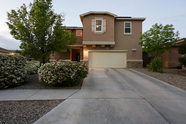 traditional-style home featuring concrete driveway, an attached garage, stone siding, and stucco siding