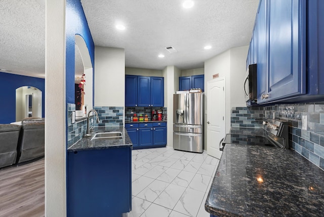 kitchen with a sink, arched walkways, blue cabinetry, a textured ceiling, and stainless steel appliances