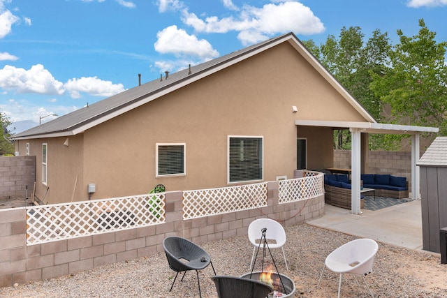 rear view of property featuring an outdoor living space with a fire pit, a patio, stucco siding, and fence
