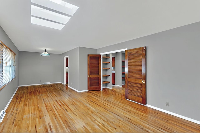 unfurnished living room with a skylight, visible vents, baseboards, and light wood finished floors
