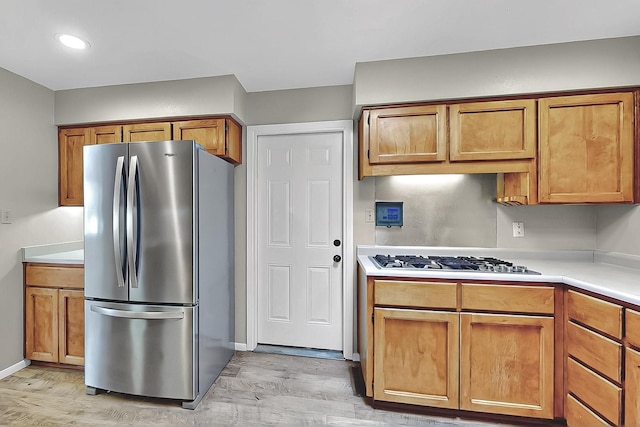 kitchen featuring light countertops, appliances with stainless steel finishes, brown cabinetry, and light wood-type flooring