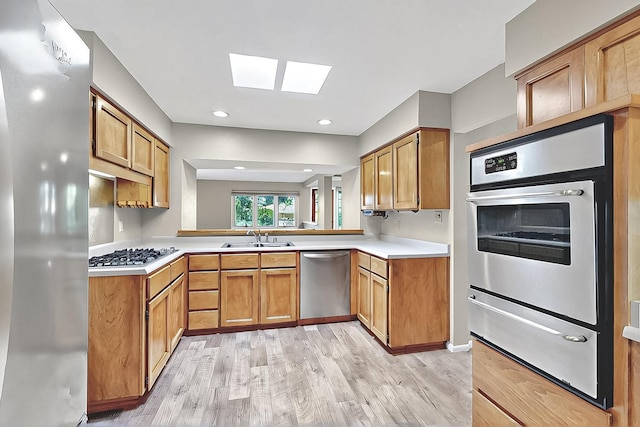 kitchen featuring a skylight, appliances with stainless steel finishes, a sink, light wood finished floors, and a warming drawer