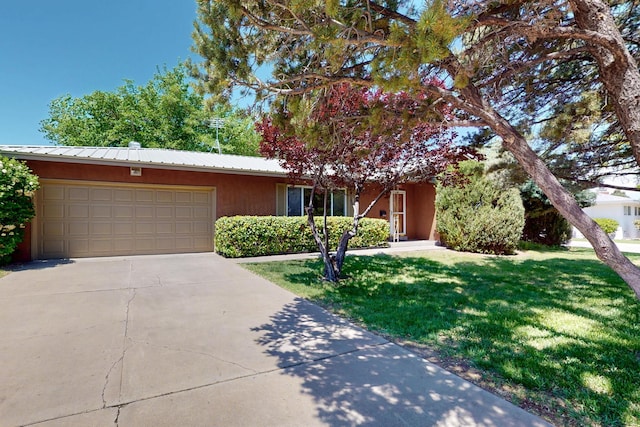 view of front of home featuring an attached garage, stucco siding, a front yard, driveway, and metal roof