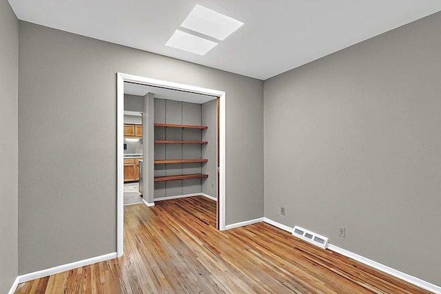 unfurnished room with a skylight, visible vents, baseboards, and light wood finished floors