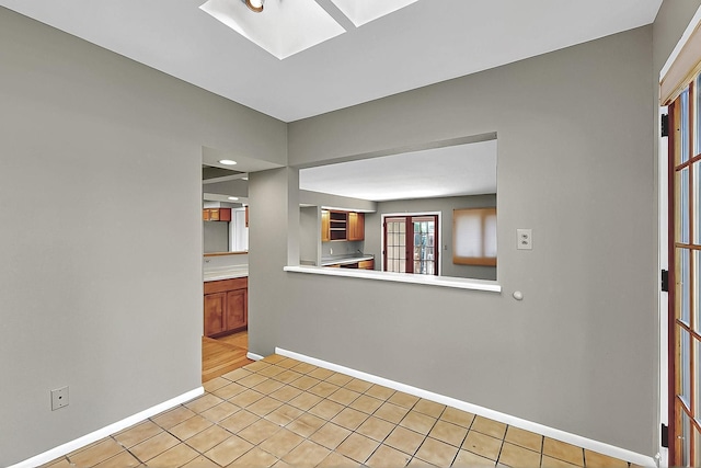 empty room with baseboards, light tile patterned floors, and a skylight