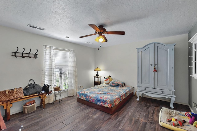 bedroom with ceiling fan, a textured ceiling, baseboards, dark wood-type flooring, and visible vents