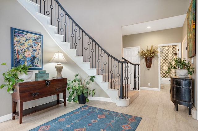 staircase with baseboards, recessed lighting, wood finished floors, and a towering ceiling