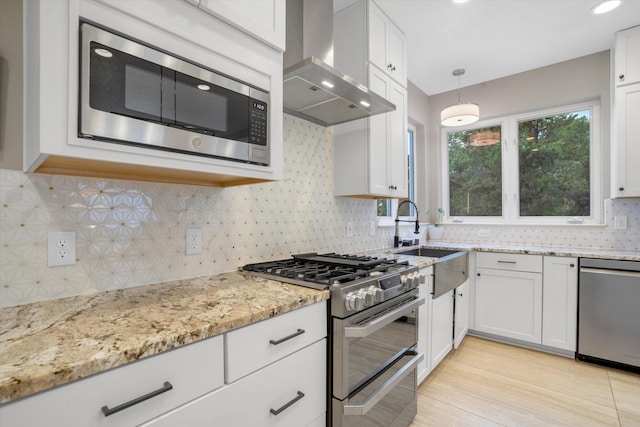 kitchen featuring white cabinets, a sink, wall chimney exhaust hood, stainless steel appliances, and backsplash