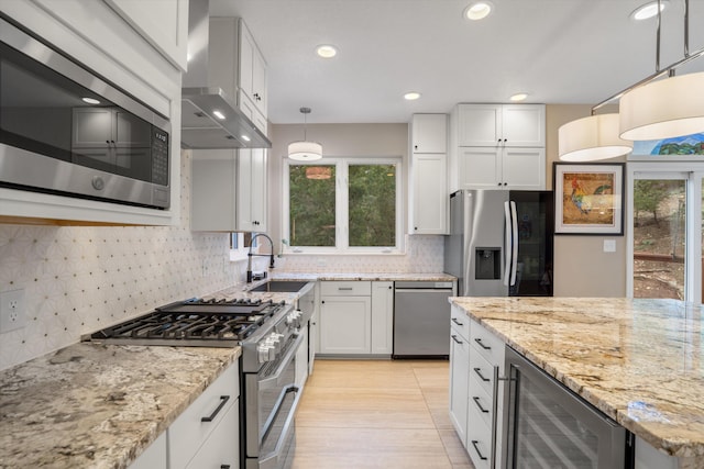 kitchen featuring wall chimney range hood, appliances with stainless steel finishes, a sink, beverage cooler, and recessed lighting