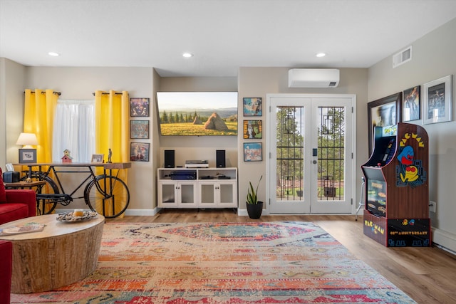 playroom featuring visible vents, wood finished floors, a healthy amount of sunlight, an AC wall unit, and french doors