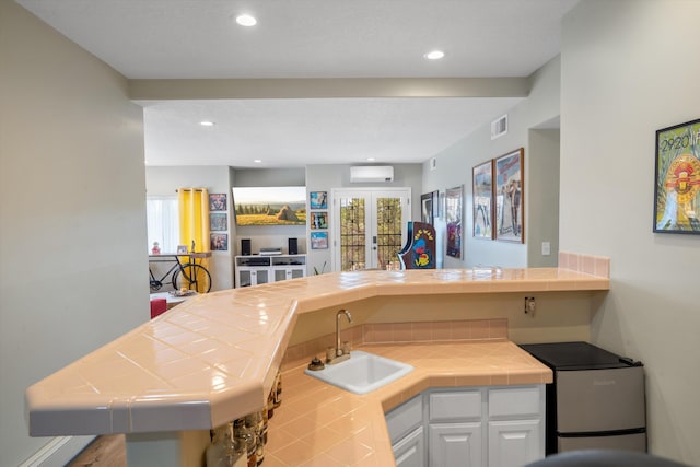 kitchen featuring white cabinets, tile countertops, visible vents, and a sink