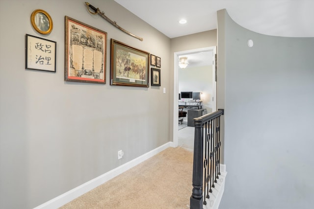 hallway featuring baseboards, an upstairs landing, and light colored carpet