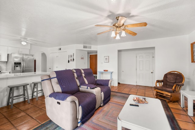 living area featuring a ceiling fan, arched walkways, tile patterned flooring, and a textured ceiling