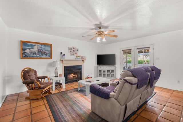 living area with tile patterned flooring, ceiling fan, a textured ceiling, a warm lit fireplace, and baseboards