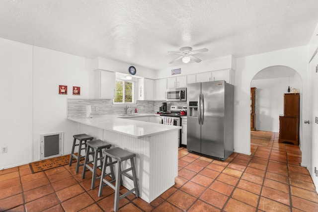 kitchen featuring stainless steel appliances, a peninsula, a kitchen bar, a sink, and a ceiling fan