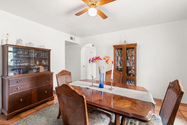 dining area featuring arched walkways, a ceiling fan, and light tile patterned floors