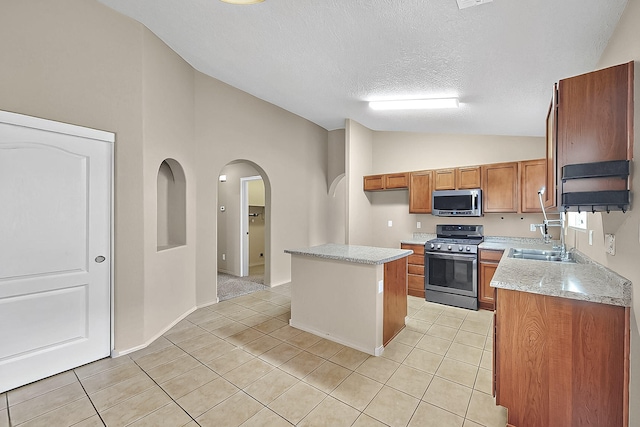 kitchen featuring appliances with stainless steel finishes, vaulted ceiling, brown cabinetry, a textured ceiling, and light tile patterned floors