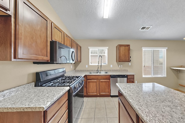 kitchen with appliances with stainless steel finishes, a sink, brown cabinets, a textured ceiling, and light tile patterned floors