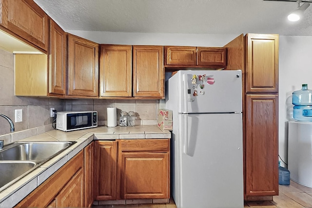 2800 Vail Ave SE Unit D113, Albuquerque, NM 87106 - kitchen with freestanding refrigerator, a sink, brown cabinets, and a textured ceiling