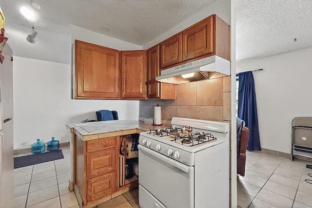2800 Vail Ave SE Unit D113, Albuquerque, NM 87106 - kitchen with gas range gas stove, under cabinet range hood, a textured ceiling, light tile patterned floors, and tile countertops