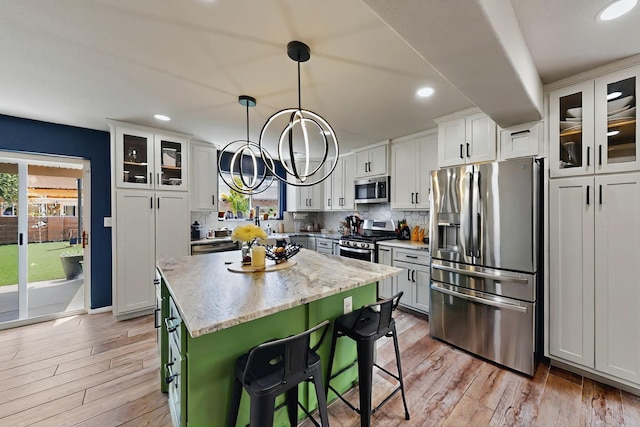 7720 Red Finch Ct NW, Albuquerque, NM 87114 - kitchen with appliances with stainless steel finishes, light wood-style flooring, a kitchen island, a kitchen bar, and decorative backsplash