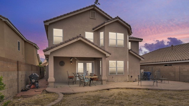4212 Caprock Rd NW, Albuquerque, NM 87114 - back of house at dusk with french doors, stucco siding, a fenced backyard, a patio area, and a tiled roof