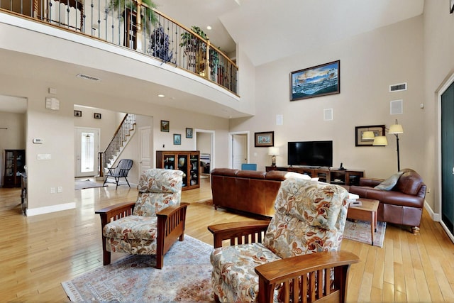 living room with a towering ceiling, stairs, light wood-type flooring, and baseboards
