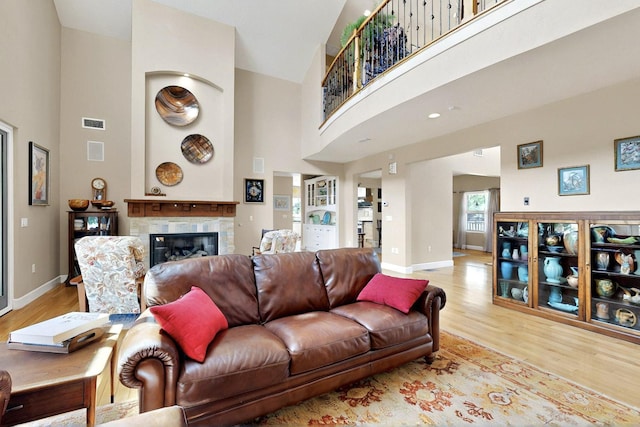 living area featuring a high ceiling, light wood-style flooring, baseboards, and a glass covered fireplace