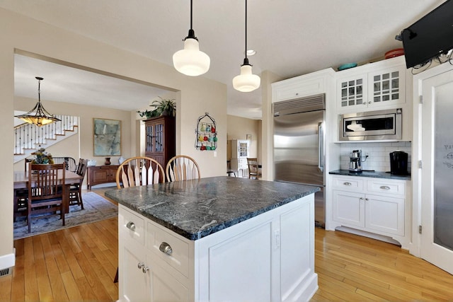 kitchen with built in appliances, light wood-type flooring, white cabinetry, and decorative backsplash