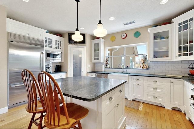 kitchen with built in appliances, dark countertops, white cabinetry, a kitchen island, and decorative backsplash