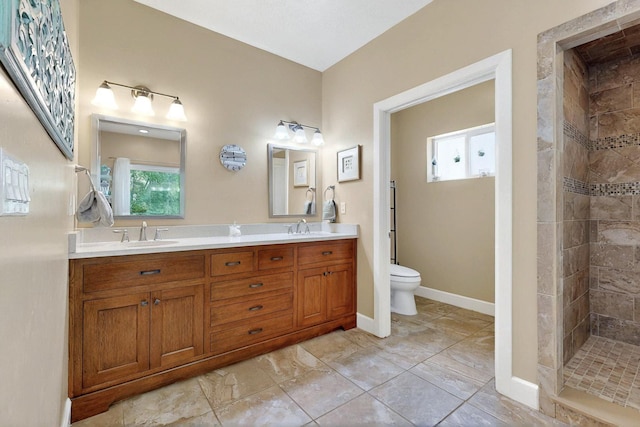 bathroom featuring toilet, tiled shower, double vanity, and baseboards
