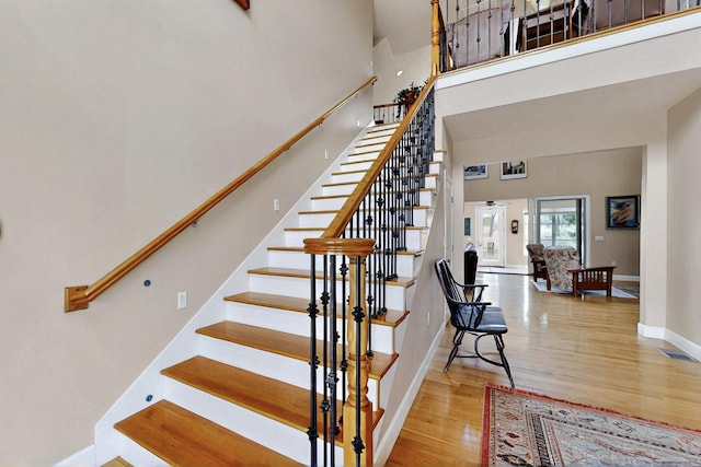 staircase featuring wood finished floors, a towering ceiling, and baseboards