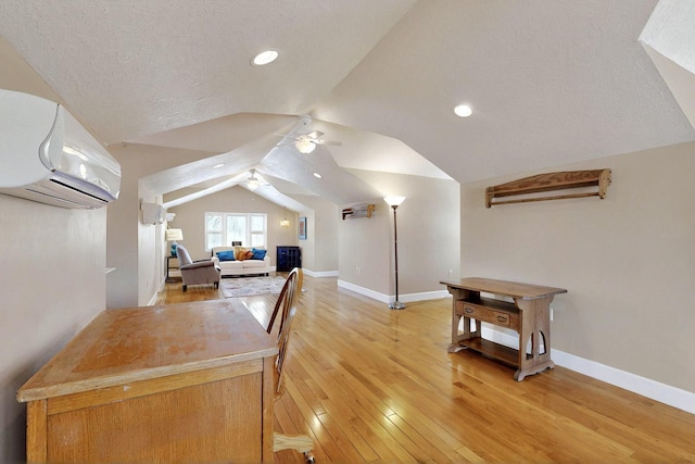 office space with a wall unit AC, lofted ceiling, light wood finished floors, baseboards, and ceiling fan