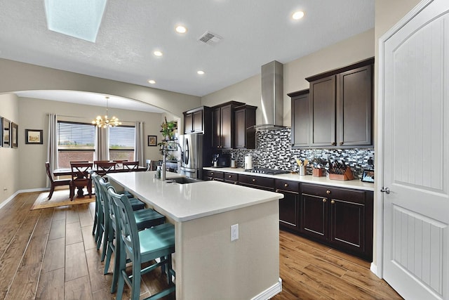 7241 Aldan Dr NE, Rio Rancho, NM 87144 - kitchen with wall chimney exhaust hood, arched walkways, black stovetop, freestanding refrigerator, and a kitchen island with sink