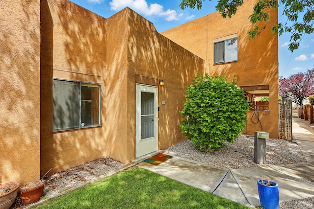 doorway to property featuring stucco siding and fence
