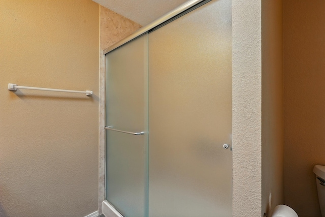 bathroom with a shower stall, toilet, and a textured wall