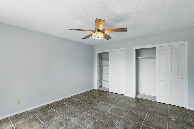 unfurnished bedroom with two closets, a textured ceiling, dark tile patterned floors, a ceiling fan, and baseboards