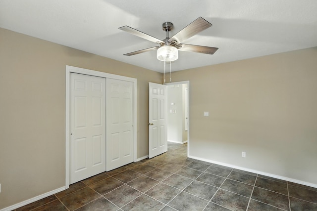 unfurnished bedroom featuring a closet, baseboards, dark tile patterned flooring, and ceiling fan