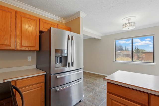 kitchen with stainless steel refrigerator with ice dispenser, light countertops, crown molding, brown cabinetry, and a textured ceiling