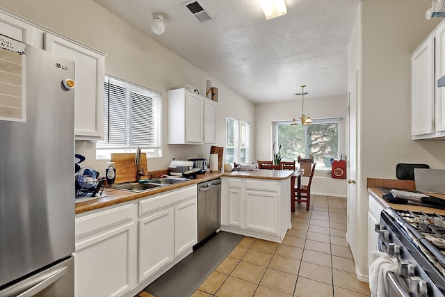 2512 Sarita Ave NW, Albuquerque, NM 87104 - kitchen featuring appliances with stainless steel finishes, a sink, white cabinets, light tile patterned flooring, and hanging light fixtures