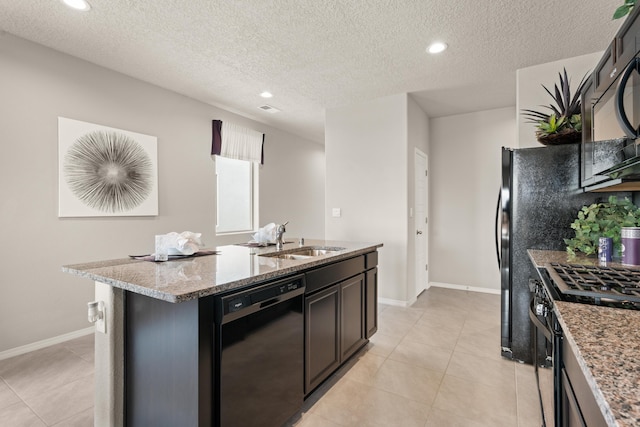 kitchen featuring black appliances, a sink, a kitchen island with sink, light stone countertops, and baseboards