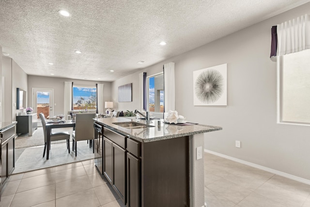 kitchen with a sink, dark brown cabinets, a textured ceiling, light stone countertops, and open floor plan